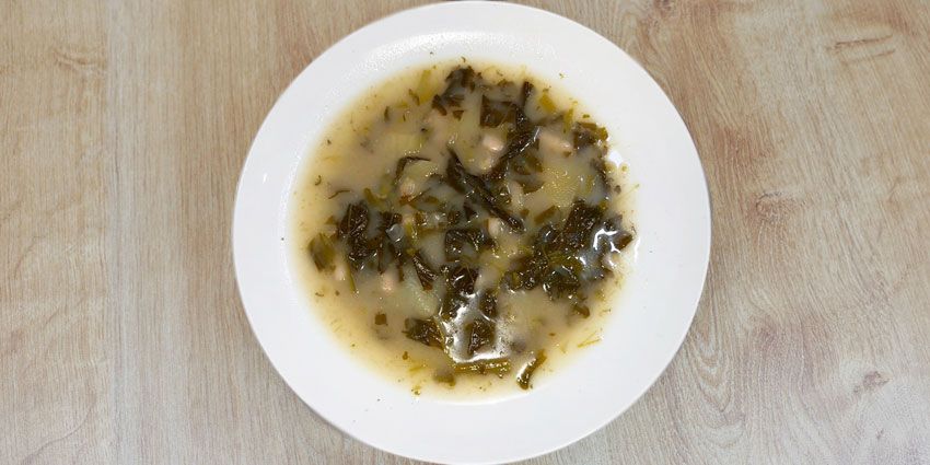 Plato hondo de caldo gallego con grelos y alubias blancas sobre una mesa de madera
