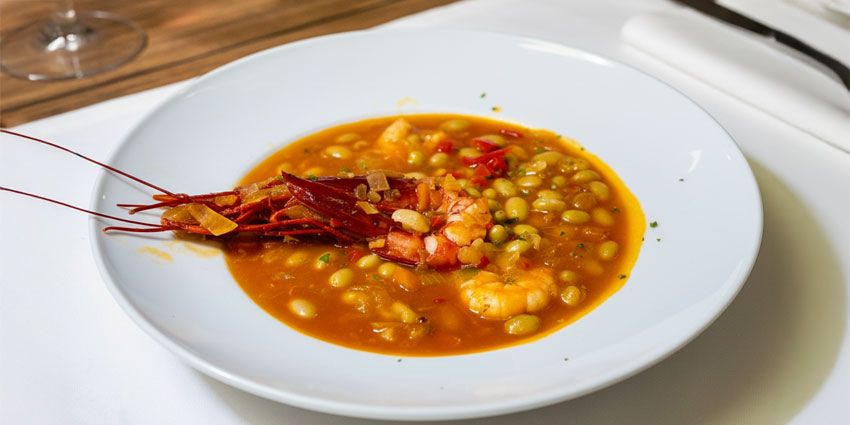 Plato hondo de pochas guisadas con un carabinero y langostinos en caldo anaranjado