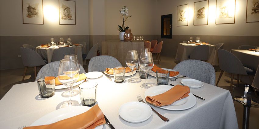 Comedor de Flor de Galicia con mesas vestidas de blanco, servilletas naranjas y cuadros en las paredes